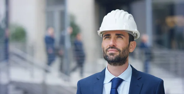 Ingenjör med hjälmens konstruktion, ler stolt av dess konstruktion som nyligen ingåtts, i bakgrunden är den inbyggda skyskrapan. Koncept: byggande, ekonomi, framtiden, passion och teknik. — Stockfoto