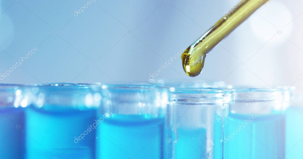 In a laboratory, a scientist with a pipette analyzes a colored liquid to extract the DNA and molecules in the test tubes. Concept: research, biochemistry, nature, pharmaceutical medicine