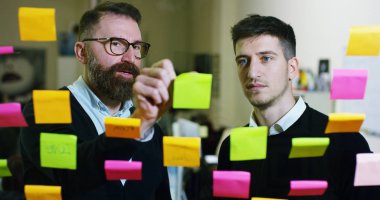 İki yaratıcı ve düşünceli bir yaratıcı ajansı ile cam ve çalışma insanların arkasına asılı renkli ve planlama notları. Konsept: takım çalışması, ajansı, yaratıcı, iş