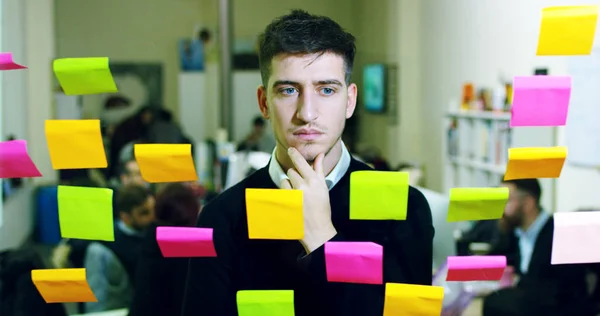 Portret van een lachende man in een doordacht en creatief bureau met kleurrijke notities en planning hangend achter het glas en de werkende mensen. Concept: teamwork, bureau, creatief, bedrijf — Stockfoto