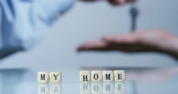 Macro cámara lenta de la palabra "Inicio" hecha de los bloques de letras de madera y detrás del comprador de la nueva casa se reciben las llaves de la casa. Concepto: nuevo hogar, futuro, nueva generación . — Foto de Stock