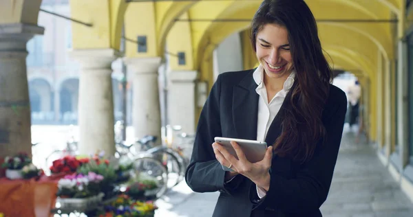 A beautiful career woman uses tablet or smartphone, in the background the city. The businesswoman smiles as she reads emails and messages work. Concept: technology, business, tablet