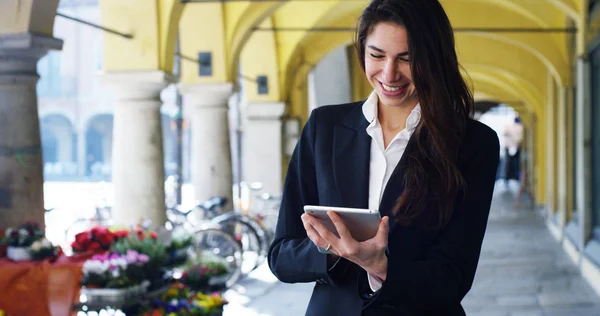 Una hermosa mujer de carrera utiliza tableta o teléfono inteligente, en el fondo de la ciudad. La empresaria sonríe mientras lee correos electrónicos y mensajes de trabajo. Concepto: tecnología, negocio, tableta — Foto de Stock