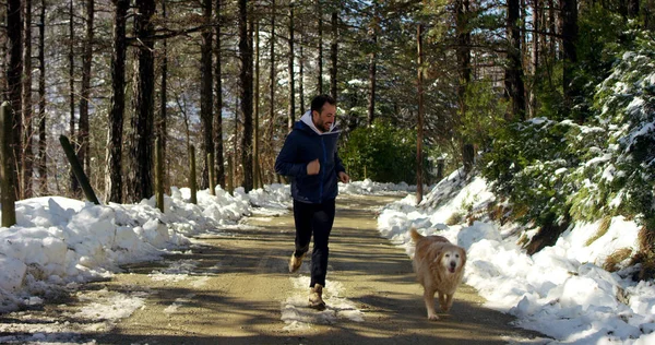 Beautiful young man runs for passion with his inseparable dog friend in the woods and is melting the first snow of the mountains rich in vegetation — Stock Photo, Image