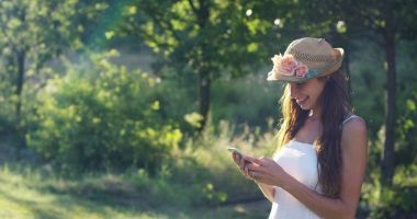 Güneşli bir günde güzel bir kadın alarak resimler veya ileti yazarak ve cep telefonunuzu kullanarak telefon akıllı telefon, onun akıllı telefon ile görüntülü görüşme sırasında gülümseyen tezahürat. bağlantı kavramı bağlantısı