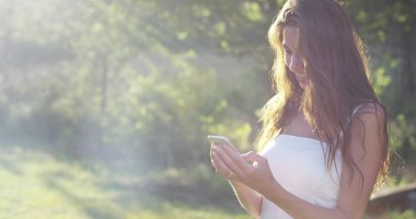 Güneşli bir günde güzel bir kadın alarak resimler veya ileti yazarak ve cep telefonunuzu kullanarak telefon akıllı telefon, onun akıllı telefon ile görüntülü görüşme sırasında gülümseyen tezahürat. bağlantı kavramı bağlantısı
