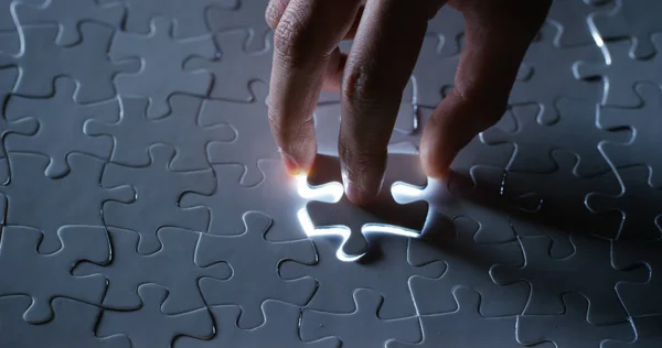 Um criativo completa o quebra-cabeça de luz preto ou branco colocando a última peça em falta. Conceito: cooperação, trabalho em equipe, criatividade e solução de acesso . — Fotografia de Stock