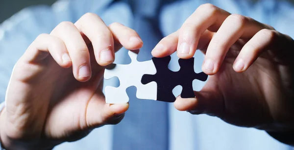 A businessman in a suit holding a white puzzle piece and a black unites them. Concept: diversity, team work, racism, and access solution.