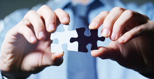 A businessman in a suit holding a white puzzle piece and a black unites them. Concept: diversity, team work, racism, and access solution.