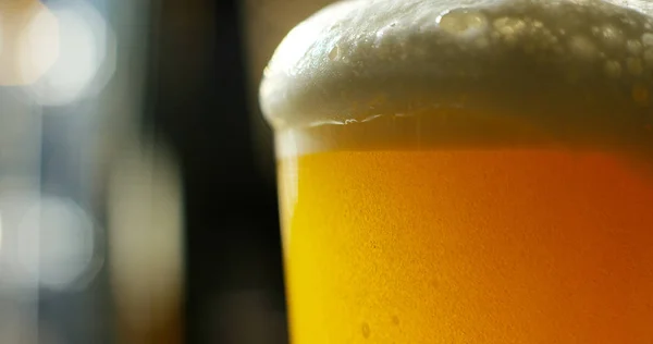 Lento movimento macro ainda vida da cerveja espumada derramado em vidro transparente isolado no fundo preto (close-up ) — Fotografia de Stock