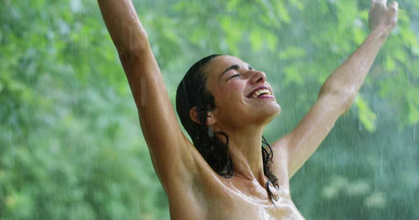 Em um dia quente de verão, uma mulher sorrindo debaixo de água cercada por vegetação. Ele refresca sob a água e sentir que seu corpo recebe o benefício da água fresca . — Fotografia de Stock