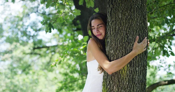 En un día soleado una mujer abrazando el árbol como un signo de amor por la naturaleza. Naturaleza que ama y protege porque el árbol es un símbolo de la vida. La mujer naturalista es despreocupada y sonriente — Foto de Stock