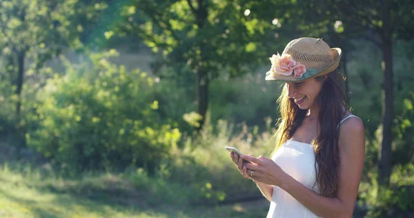 Güneşli bir günde güzel bir kadın alarak resimler veya ileti yazarak ve cep telefonunuzu kullanarak telefon akıllı telefon, onun akıllı telefon ile görüntülü görüşme sırasında gülümseyen tezahürat. bağlantı kavramı bağlantısı