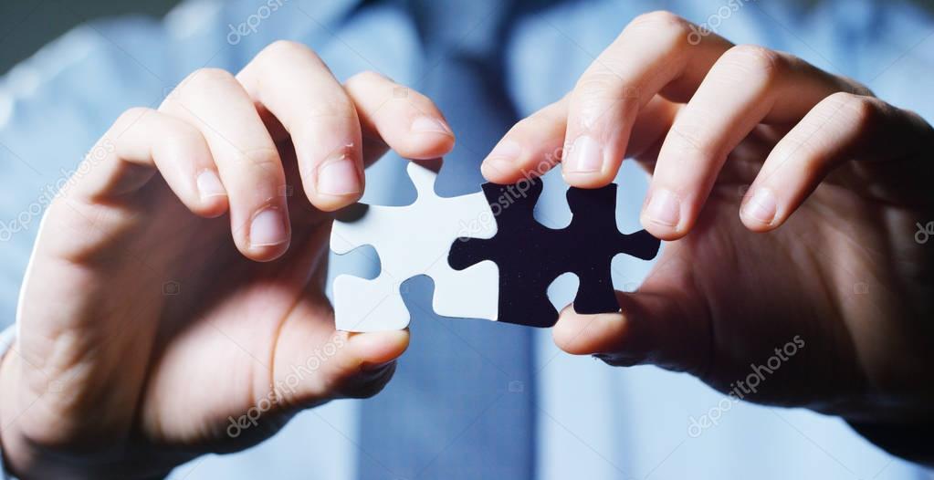 A businessman in a suit holding a white puzzle piece and a black unites them. Concept: diversity, team work, racism, and access solution.