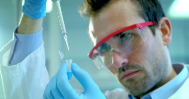 güzel genç bilim adamı erkek doktor sıvı virüs hücreleri kullanarak nitelikli ekipman ve gözleri korumak için gözlük takan ve laboratuvar bardak bakımı profesyonel Laboratuvar analiz