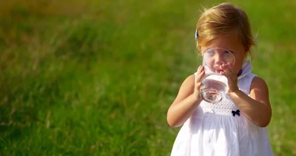 Adorável menina de dois anos de idade beber um copo de água pura e fresca olhando para a câmera e sorrir com atmosfera cheia de vida. conceito de água pura. vida de saúde e crianças felizes rindo — Fotografia de Stock