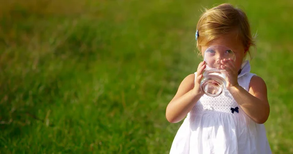Adorável menina de dois anos de idade beber um copo de água pura e fresca olhando para a câmera e sorrir com atmosfera cheia de vida. conceito de água pura. vida de saúde e crianças felizes rindo — Fotografia de Stock