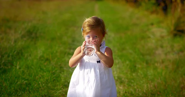 Adorable niña de dos años bebe un vaso de agua pura y fresca mirando a la cámara y sonríe con un ambiente lleno de vida. concepto de agua pura. la vida de salud y niños felices riendo — Foto de Stock