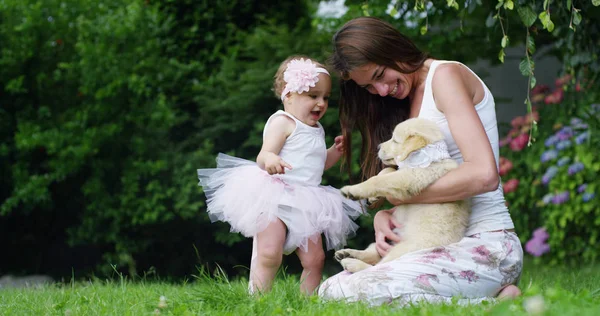 Tendre mère avec un enfant jouant avec un chiot doux golden retriever dans un beau jardin par une journée ensoleillée couché sur l'herbe — Photo