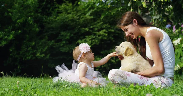 Tendre mère avec un enfant jouant avec un chiot doux golden retriever dans un beau jardin par une journée ensoleillée couché sur l'herbe — Photo