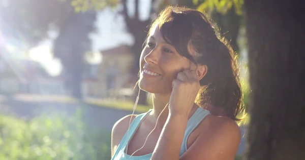 Una chica feliz ajuste relajado trotar y correr en una calle con árboles y naturaleza, el uso de auriculares para la música y correr lento en la puesta de sol. concepto de felicidad para el deporte y la relajación fitness en la naturaleza — Foto de Stock