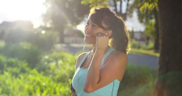 Une fille heureuse fit du jogging détendu et courir dans une rue avec des arbres et de la nature, en utilisant des écouteurs pour la musique et courir lentement au coucher du soleil. concept de bonheur pour le sport et la relaxation fitness dans la nature — Photo