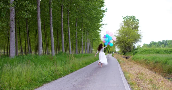 Chica de belleza con cabello largo saludable al aire libre. Feliz joven sonriente disfrutando de la naturaleza. Hermosa joven divirtiéndose con globos en el prado. Concepto de libertad. Puesta de sol — Foto de Stock