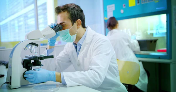 Ilmuwan muda yang baik hati dokter laki-laki menganalisis sel-sel virus cair di laboratorium profesional menggunakan peralatan yang berkualitas dan memakai kacamata untuk melindungi mata dan merawat kacamata lab — Stok Foto