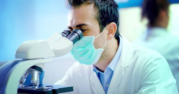 Ilmuwan muda yang baik hati dokter laki-laki menganalisis sel-sel virus cair di laboratorium profesional menggunakan peralatan yang berkualitas dan memakai kacamata untuk melindungi mata dan merawat kacamata lab — Stok Foto