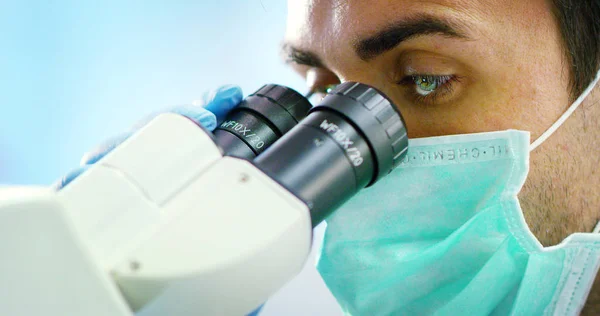 Хороший молодой ученый врач мужского пола, анализирующий вирусные клетки жидкостей в профессиональной лаборатории, используя квалифицированное оборудование и очки для защиты глаз и ухода за лабораторными очками — стоковое фото