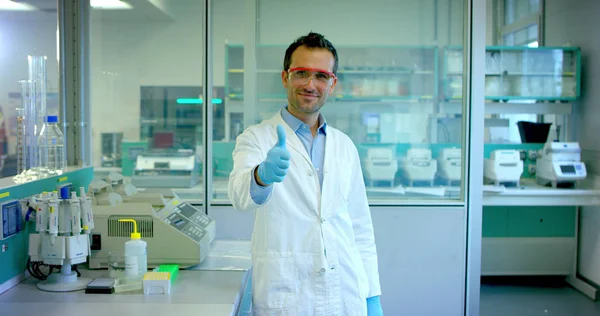 Bom jovem cientista médico masculino analisando células de vírus líquidos em laboratório profissional usando equipamentos qualificados e vestindo óculos para proteger os olhos e cuidar dos óculos de laboratório — Fotografia de Stock