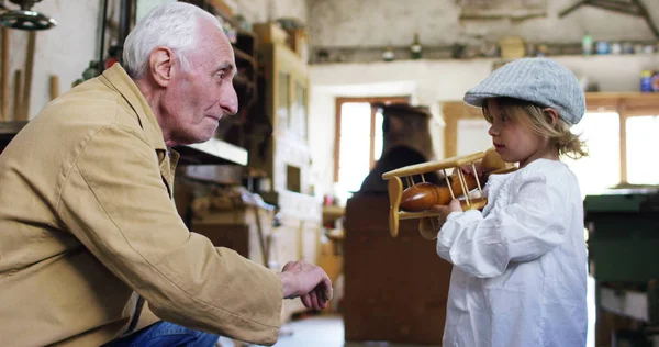 Di sebuah toko kayu tua seorang anak dan kakek bermain dengan konsep pesawat kayu tradisi yang terus berlanjut dari waktu ke waktu dan kejutan — Stok Foto