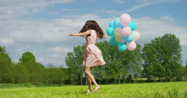 Chica de belleza con cabello largo saludable al aire libre. Feliz joven sonriente disfrutando de la naturaleza. Hermosa joven divirtiéndose con globos en el prado. Concepto de libertad. Puesta de sol — Foto de Stock