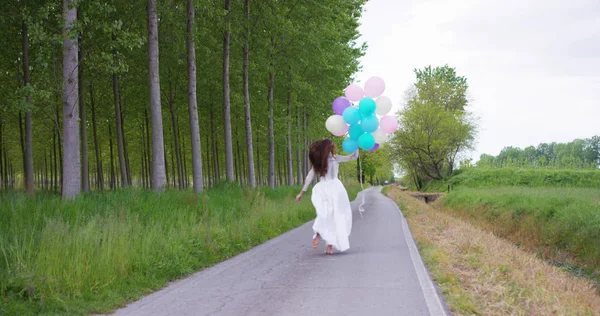 Chica de belleza con cabello largo saludable al aire libre. Feliz joven sonriente disfrutando de la naturaleza. Hermosa joven divirtiéndose con globos en el prado. Concepto de libertad. Puesta de sol — Foto de Stock