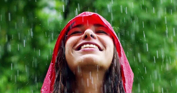 A rapariga sorri e ri-se à chuva. a chuva cai, as gotas caem em seu rosto e a menina está feliz com a vida e a natureza ao redor. conceito de natureza e vida feliz. Aventura, pureza . — Fotografia de Stock