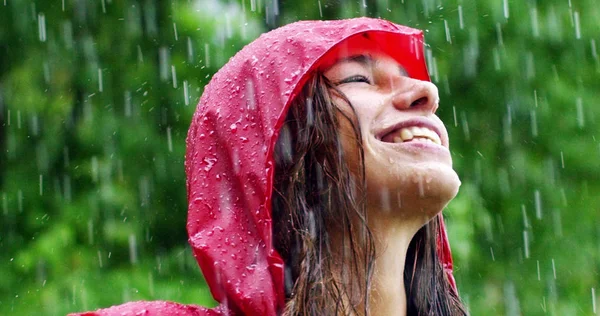 A rapariga sorri e ri-se à chuva. a chuva cai, as gotas caem em seu rosto e a menina está feliz com a vida e a natureza ao redor. conceito de natureza e vida feliz. Aventura, pureza . — Fotografia de Stock