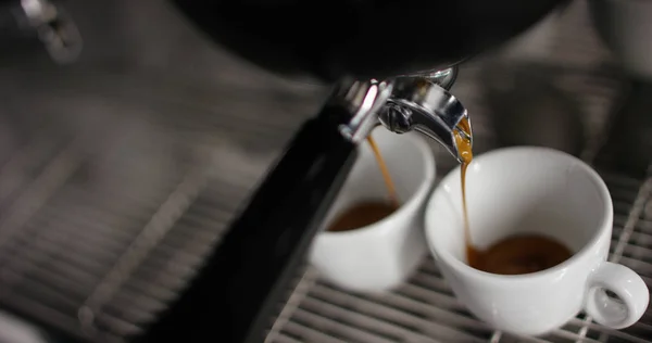 Super Zeitlupe von heißem Espresso, der in zwei weiße Porzellantassen aus der Kaffeemaschine in 4k gegossen wird (Nahaufnahme von oben)) — Stockfoto