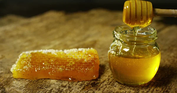 biological and genuine honey drips inside a jar. I honeycomb dripping honey. black background and a wooden table. honey falls in slowmotion and it was done by honeybees from Australia.