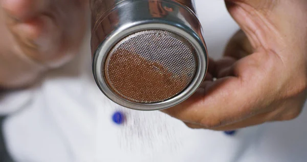 Un confitero profesional espolvorea postres de cacao o caramelos de chocolate sobre dulces, haciéndolos sabrosos y hermosos. Concepto: la producción de dulces, crema, chocolate, aire delicioso, gourmet . —  Fotos de Stock