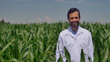 Kameraya gülümseyen bir çiftçinin portresi, mısır tarlasına bakıyor ve kontrol ediyor, yeşillikler arka planda. Kavram: ekoloji, mısır, biyolojik ürün, teftiş, su, doğal ürünler, profesyonel, çevre.