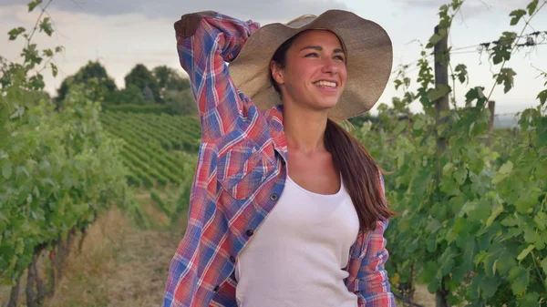 Hermosa muchacha sonriente (mujer) agricultora vigilando los campos de uva, en un sombrero de paja y en una camisa, fondo verde. Concepto ecología, vino, bio-producto, inspección, agua, productos naturales, agricultura — Foto de Stock