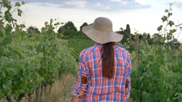 Hermosa muchacha sonriente (mujer) agricultora vigilando los campos de uva, en un sombrero de paja y en una camisa, fondo verde. Concepto ecología, vino, bio-producto, inspección, agua, productos naturales, agricultura — Foto de Stock