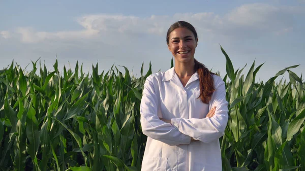 A növényvédelmi szakember, megvizsgálja a kukorica mezőket, egy fehér köpenyt, a lány (nő) mosolyog, a háttérben zöld. Koncepció: ökológia, bio termék, vizsgálat, víz, természetes termékek, szakmai, zöld — Stock Fotó