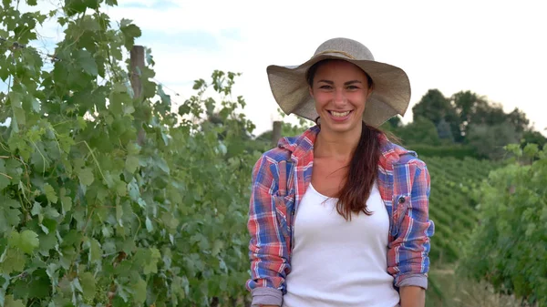 Vackra leende tjej (kvinna) bonde vakar över druva fälten, i en stråhatt och i en skjorta, gröna bakgrunden. Begreppet ekologi, vin, bio produkt, inspektion, vatten, naturliga produkter, jordbruk — Stockfoto