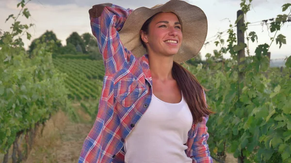 Beautiful smiling girl (woman) farmer watching over grape fields, in a straw hat and in a shirt, greens background. Concept ecology, wine, bio product, inspection, water, natural products, agriculture — Stock Photo, Image