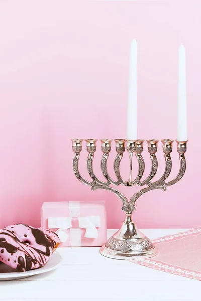 Celebração de Hanukkah, o primeiro dia. Castiçal, rosquinhas fritas e presente, sobre fundo branco e rosa — Fotografia de Stock