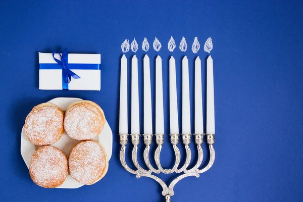 Celebração de Hanukkah. Castiçal com rosquinhas fritas, presente, em fundo branco e azul — Fotografia de Stock