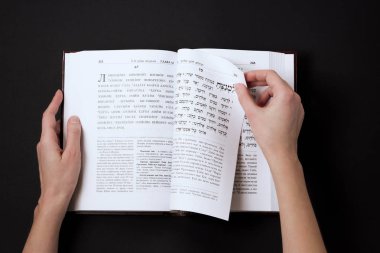 Jewish book, with womans hand, on black background. Text of the Hebrew, prayer. Woman reading book. clipart