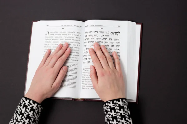 Libro judío, con mano de mujer, sobre fondo negro. Texto del hebreo, oración. Mujer reza con libro . — Foto de Stock