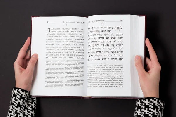 Libro judío, con mano de mujer, sobre fondo negro. Texto del hebreo, oración. Mujer leyendo libro . — Foto de Stock